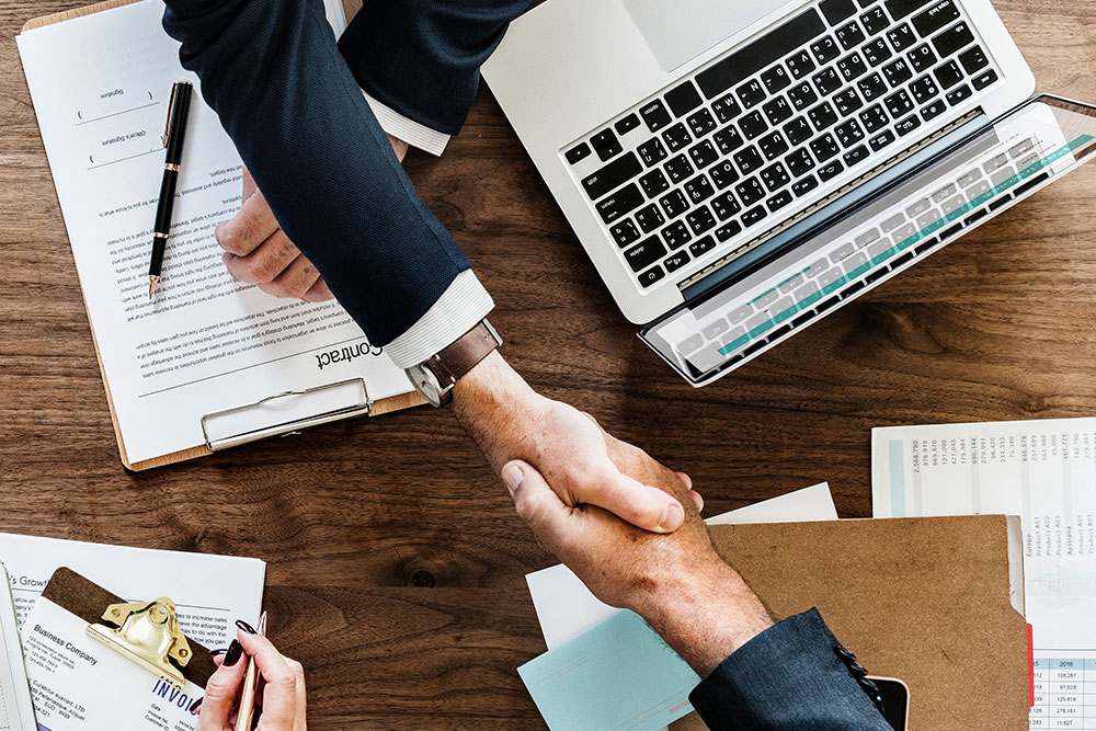 two men with laptop and papers shaking hands