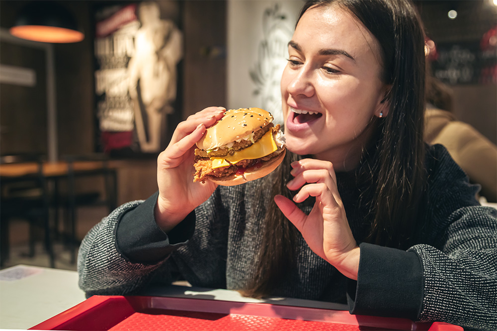 Side view of young female preparing to bite a whole tasty hamburger 