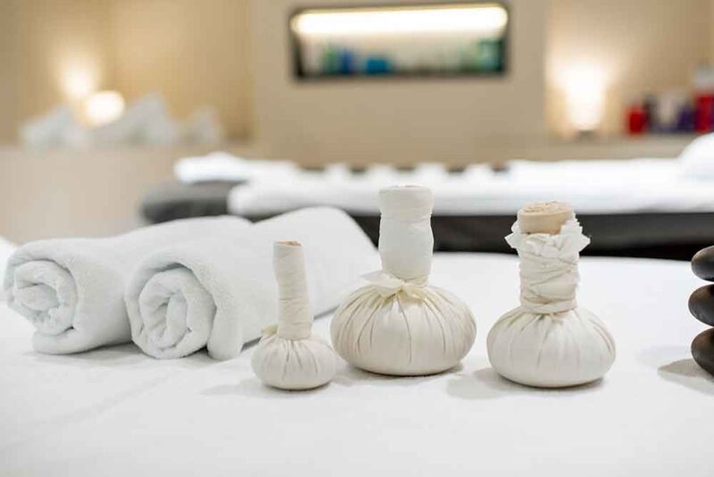 Spa essentials, including rolled towels and herbal compress balls, on a massage table in Sharjah spa. 