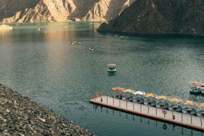 Peaceful lake surrounded by the rocky Hajar Mountains, with boats and a dock featuring shaded seats