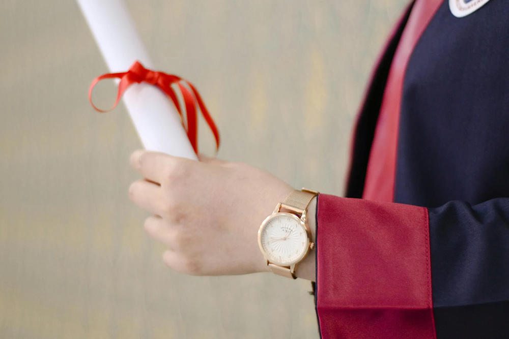 A person in black convocation gown holding a degree 