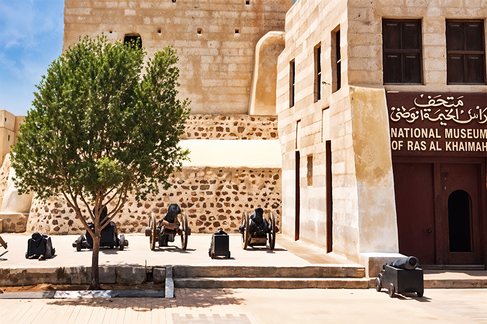 The old brown National Museum of Ras al Khaimah building has a tree standing beside it. 