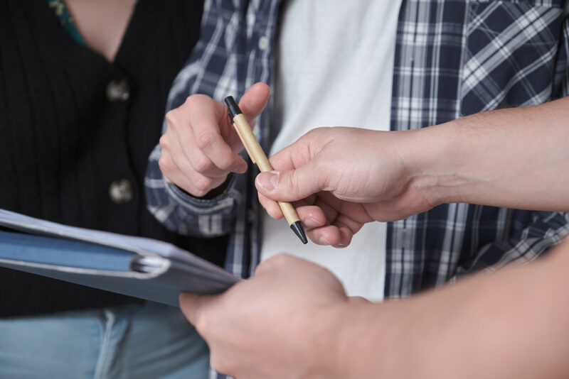 a person with papers giving a pen to the other person for signatures