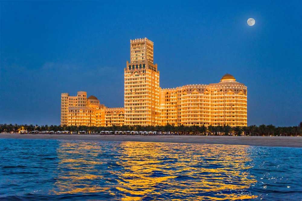  a night picture of gold-lit building with sea view. 