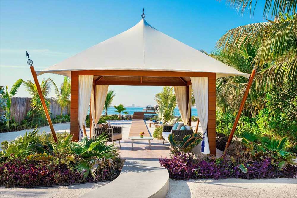 A white tent-like sitting area with beach view. and surrounding greenery 