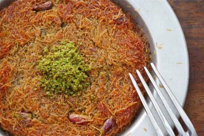 Kunafa in a silver bowl with pistachios and a fork