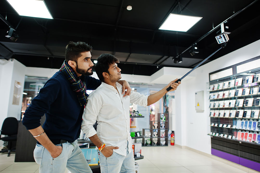 Two men making a selfie by monopod stick in a mobile shop