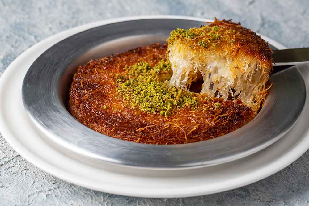 Kunafa with pistachios served in a silver bowl and  white platter 