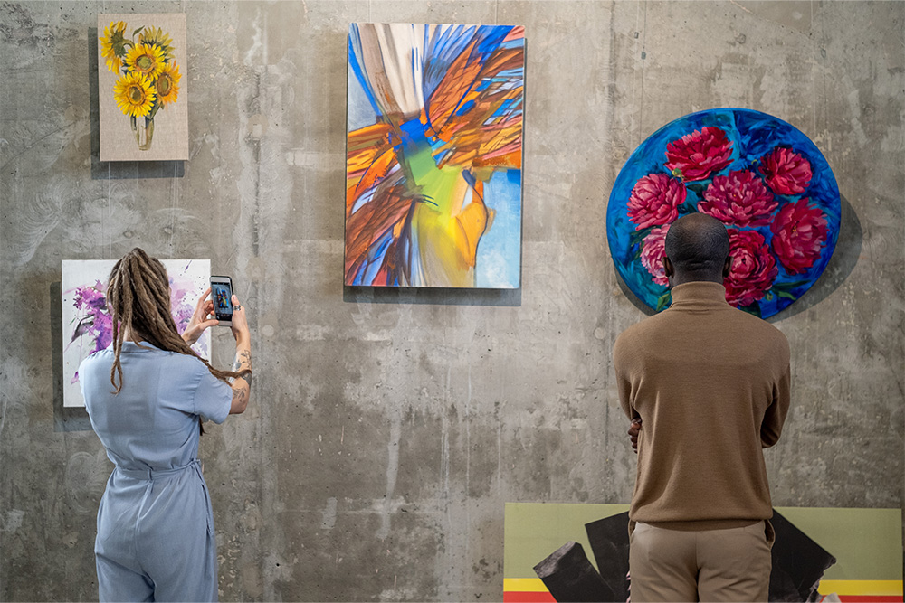 Two individuals in an art gallery observing framed paintings