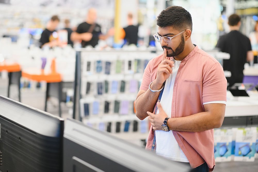 A man standing in an electronic shop to buy a smartphone 