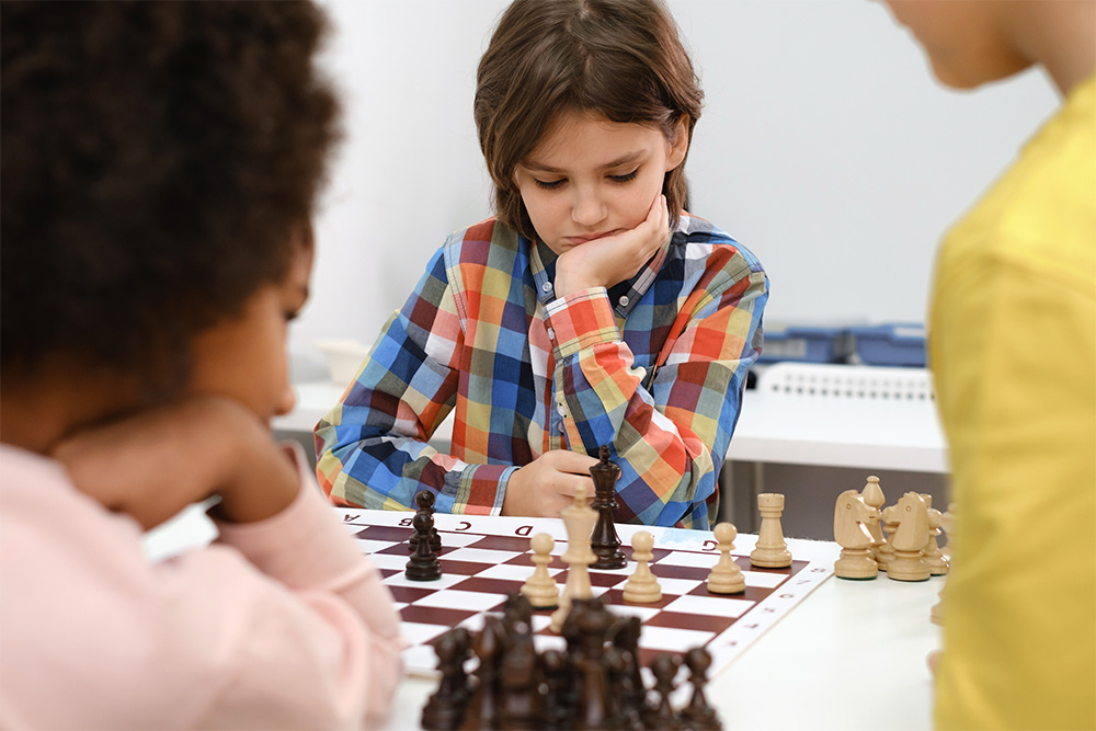 Diverse group of kids playing chess with the concentration of clever having fun at school while playing chess