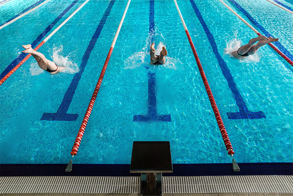 Rear view of three male swimmers diving into a swimming pool