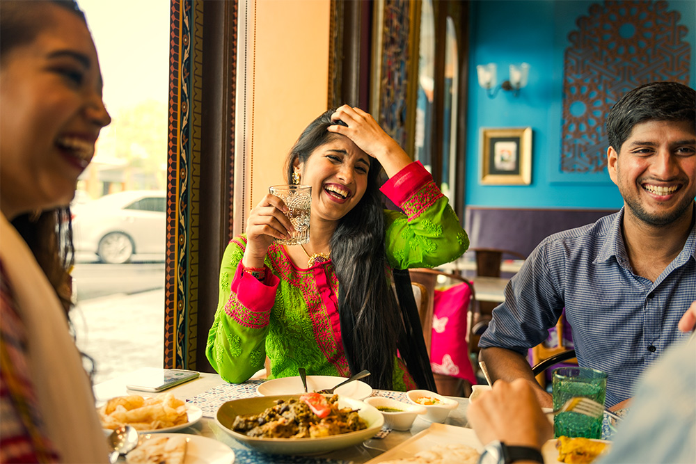 a group of friends enjoying authentic Pakistani food and laughing 