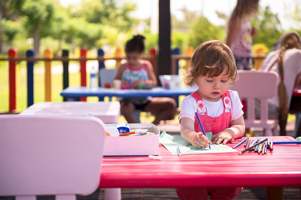 Girls are colouring in an outdoor activity space