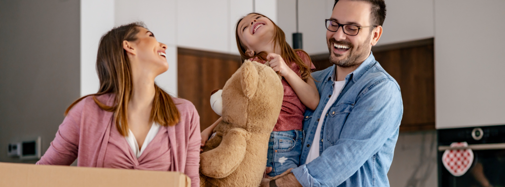 A family joyfully moving into their new home, with the father holding a teddy bear and daughter, symbolizing the excitement of finding the perfect property through building strong relationships with homeowners and developers."