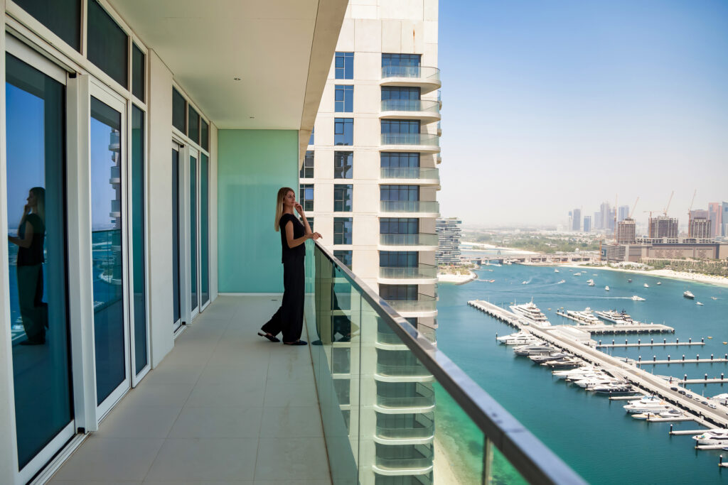 Woman standing on a balcony of a high-rise building overlooking the marina, highlighting luxury waterfront views in Dubai, relevant for a blog article titled "Securing Your Real Estate Trade License in Dubai.