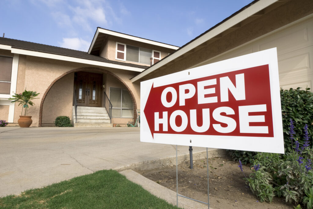 A red and white "Open House" sign is placed in front of a suburban home, directing potential buyers toward the entrance. This image illustrates the importance of hosting effective open houses to attract interested buyers and boost real estate sales.