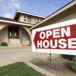 A red and white "Open House" sign is placed in front of a suburban home, directing potential buyers toward the entrance. This image illustrates the importance of hosting effective open houses to attract interested buyers and boost real estate sales.