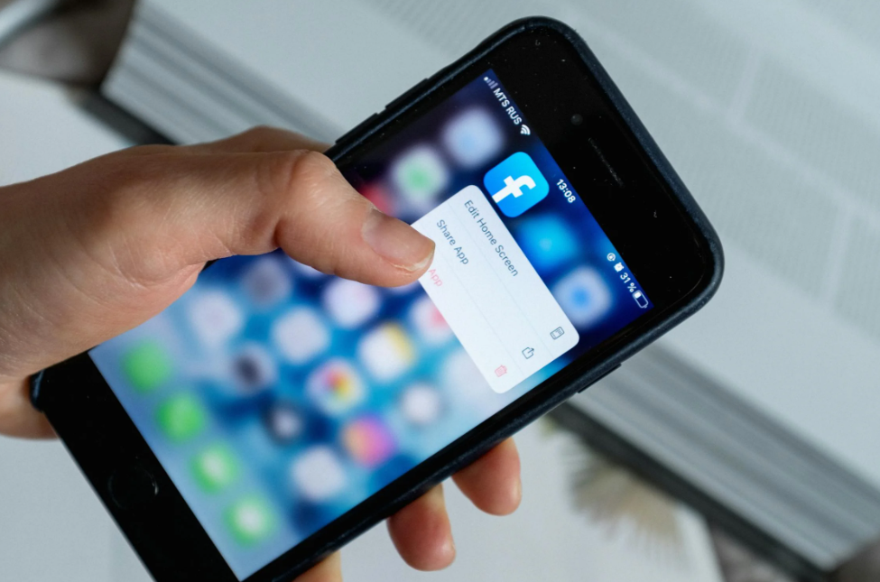 Close-up of a person holding a smartphone with the Facebook app icon displayed on the screen, highlighting the action of managing the app for social media engagement.