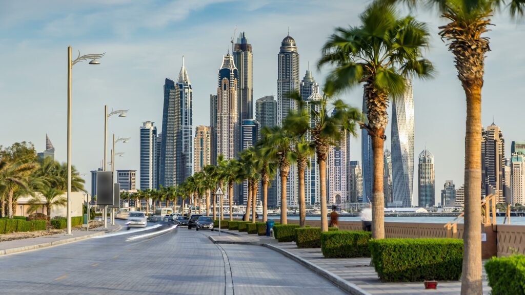 Palm tree-lined road with the Dubai Marina skyline in the background, showcasing modern skyscrapers against a clear sky.