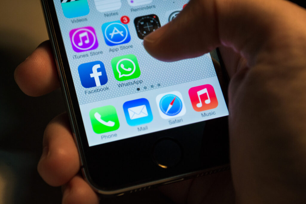 A close-up of a smartphone screen displaying popular apps, including WhatsApp, Facebook, and Mail. A person’s finger is hovering over the WhatsApp icon, highlighting the importance of using WhatsApp for lead generation. 