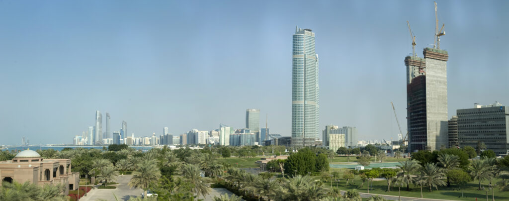 Panoramic view of Abu Dhabi's skyline featuring modern skyscrapers under construction and lush greenery, illustrating the city's rapid development and focus on urban community planning.